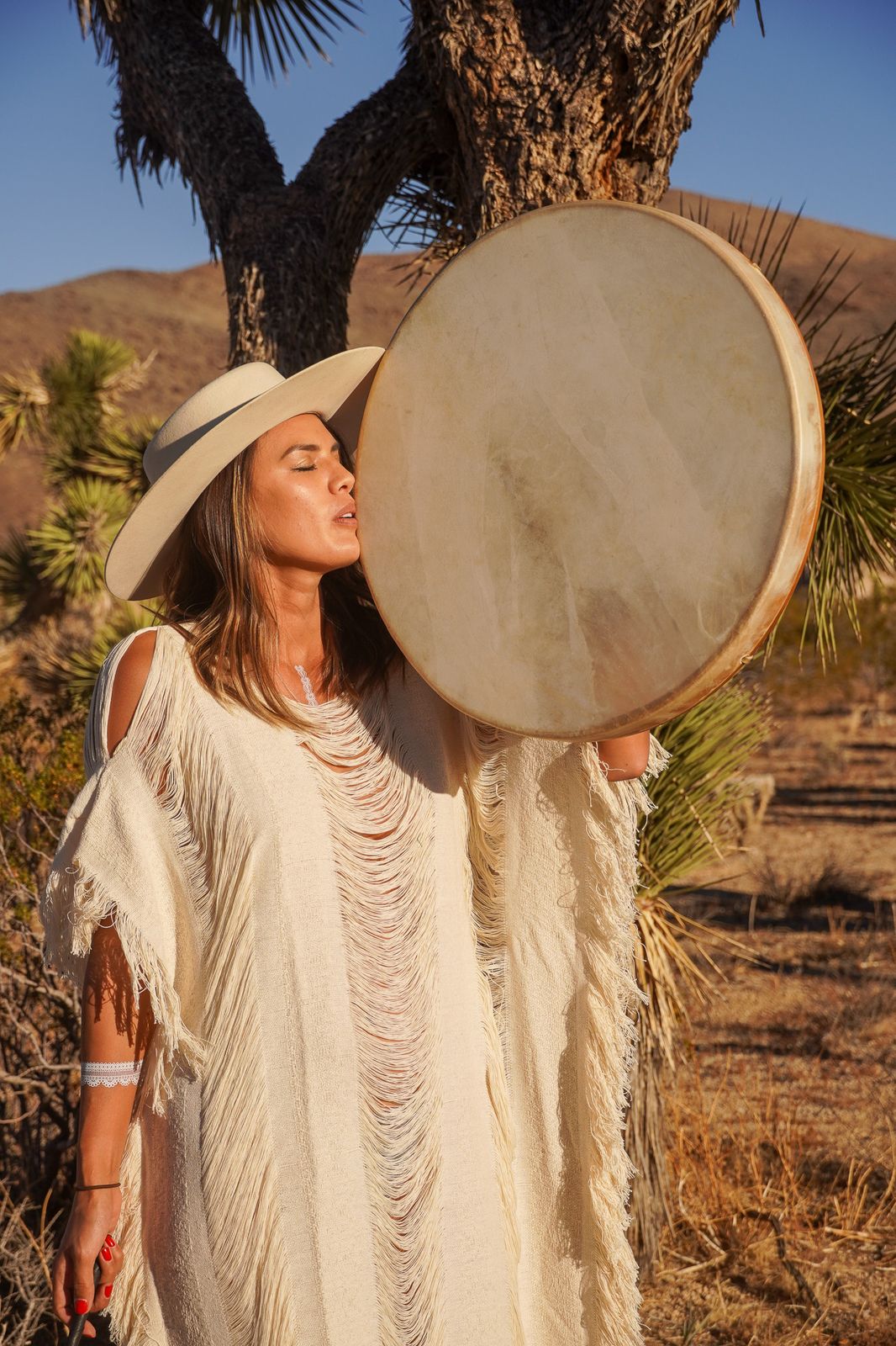 Woman in a wide-brim hat holding a large frame drum